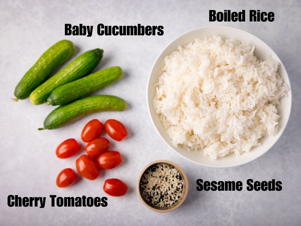 Labelled ingredients of baby cucumbers, cherry tomatoes, sesame seeds and boiled rice in a bowl on a light grey background.