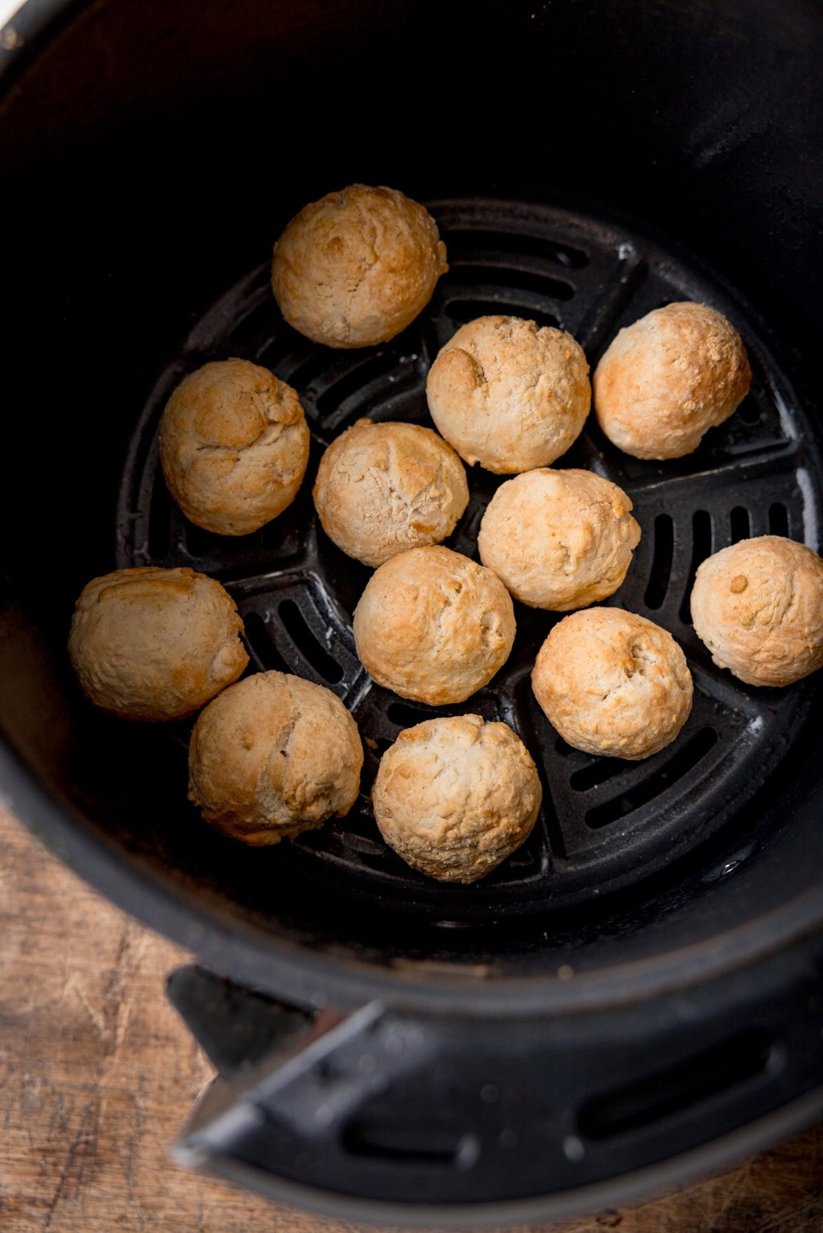 A tall, overhead shot of uncooked doughnut holes in a black air fryer basket. The air fryer basket is on top of a wooden surface.