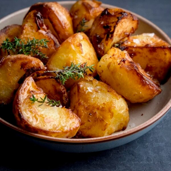 Square image of a bowl filled with Air Fryer Roast Potatoes, sprinkled with salt and parsley, on a dark blue background.