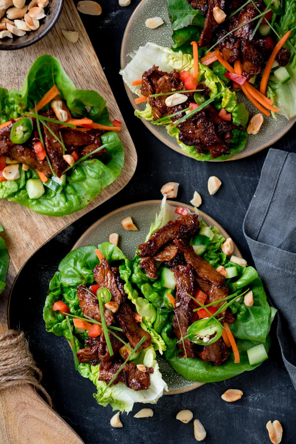 Picture of a plate with two Korean beef lettuce wraps with another plate and board with more lettuce wraps in the background.