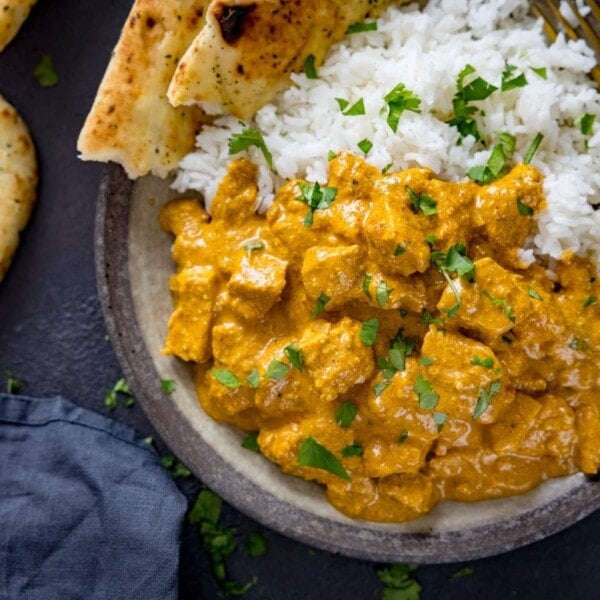 Chicken korma, naan and rice in a bowl on a dark background.