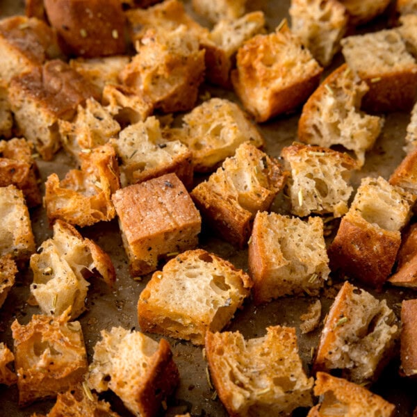 A square, close-up shot of crispy croutons. The image is of lots of crispy croutons on top of a tray lined with baking parchment, this fills the image so nothing else can be seen.