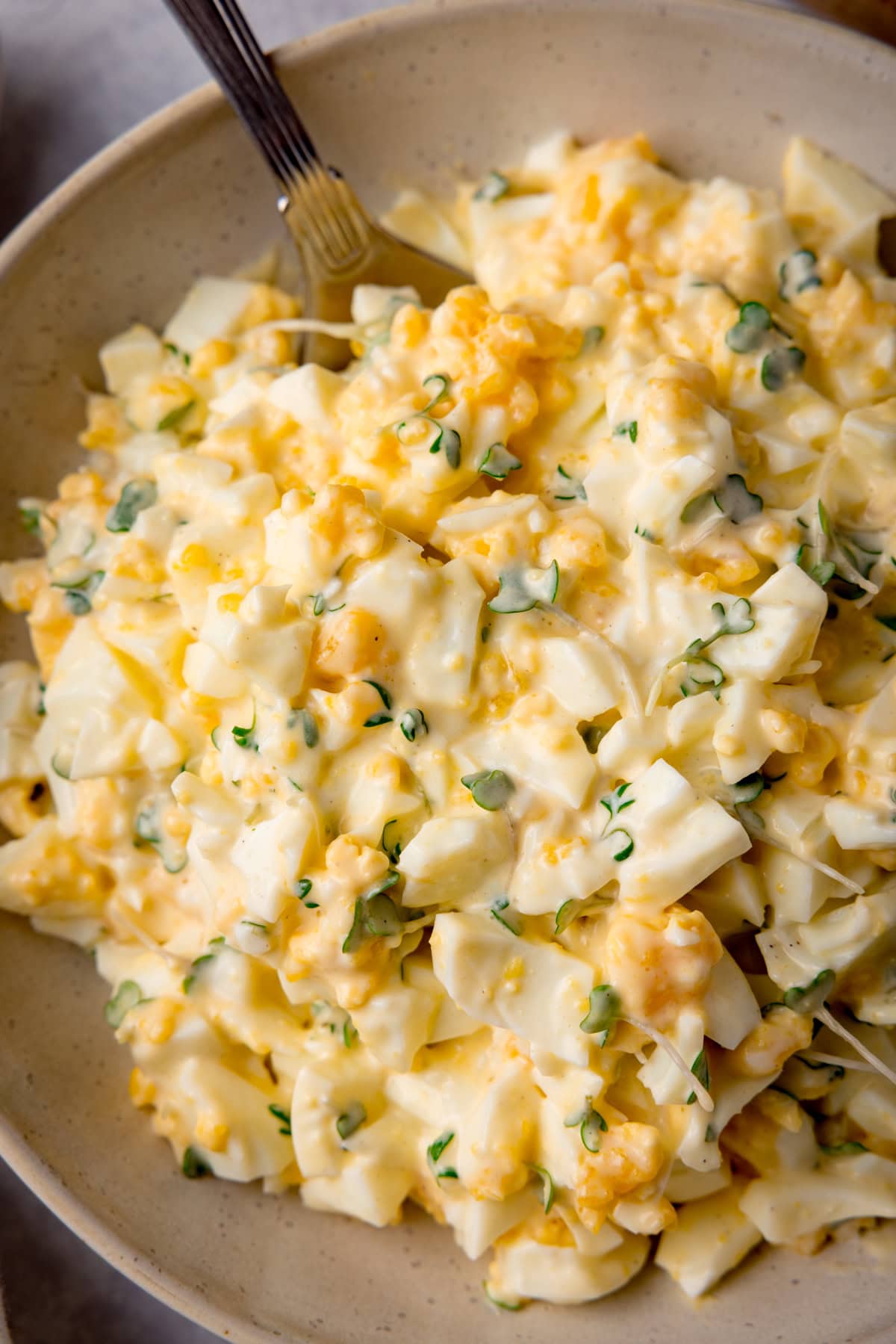 Tall overhead, close-up image of egg mayonnaise in a white bowl with a silver spoon sticking out.