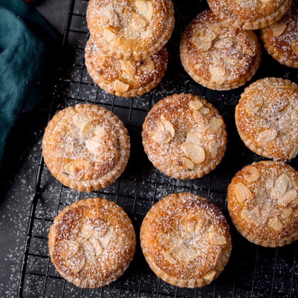 An overhead picture of some mince pies on a black wire cooling rack. All the mince pies have been dusted with icing sugar.