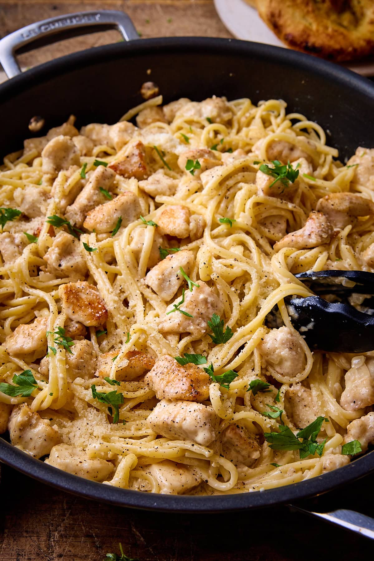 Close up picture of garlic parmesan chicken pasta in a dark grey pan sat on a wooden table.