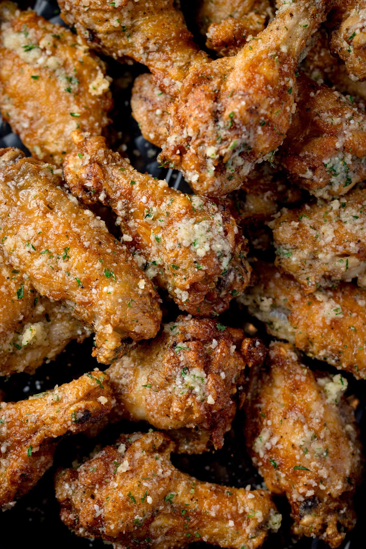 A tall, closeup shot of a pile of Garlic Parmesan Chicken Wings on a black rectangular baking tray.