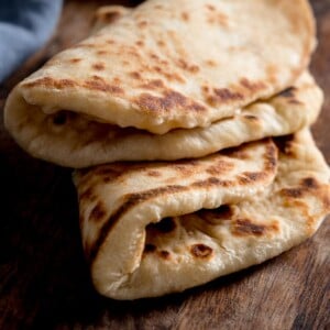 Square image of two folded flatbreads on a wooden table next to a blue napkin