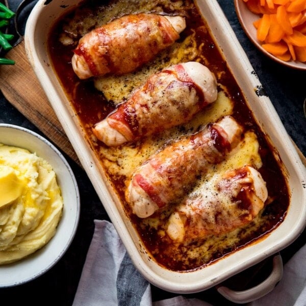 Square image of hunters chicken in a baking dish next to side dishes of mashed potatoes, carrots and green beans.