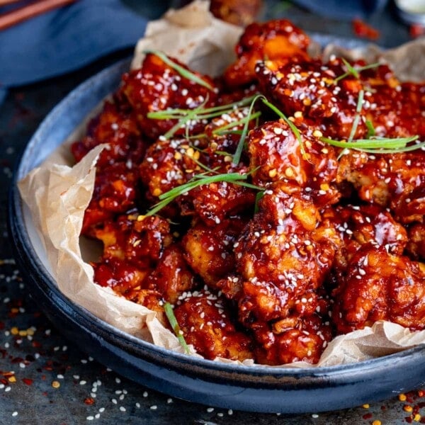 Crispy Korean chicken in a blue bowl topped with strips of spring onion