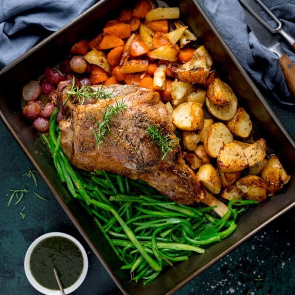 Overhead picture of a large roasting pan with a roast leg of lamb with veggies and potatoes in there too.