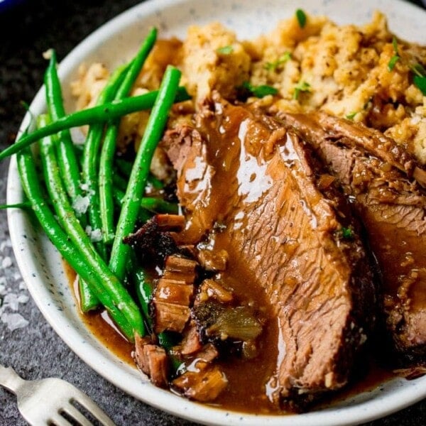 plate of sliced beef, vegetables and gravy on a dark background