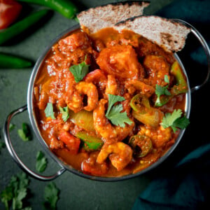 Overhead close up picture of a prawn balti curry in a balti dish on a green background.