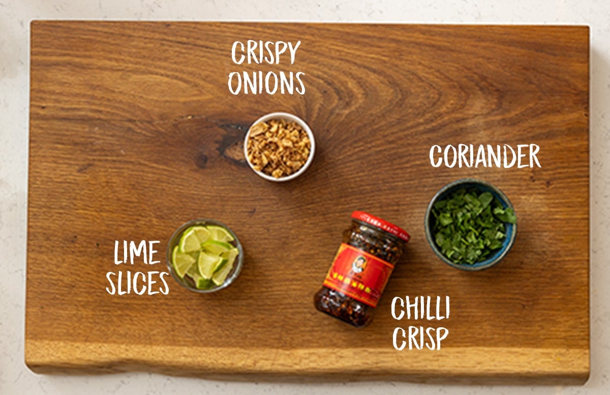 The toppings to go onto a chicken laksa soup all sat on a wooden chopping board