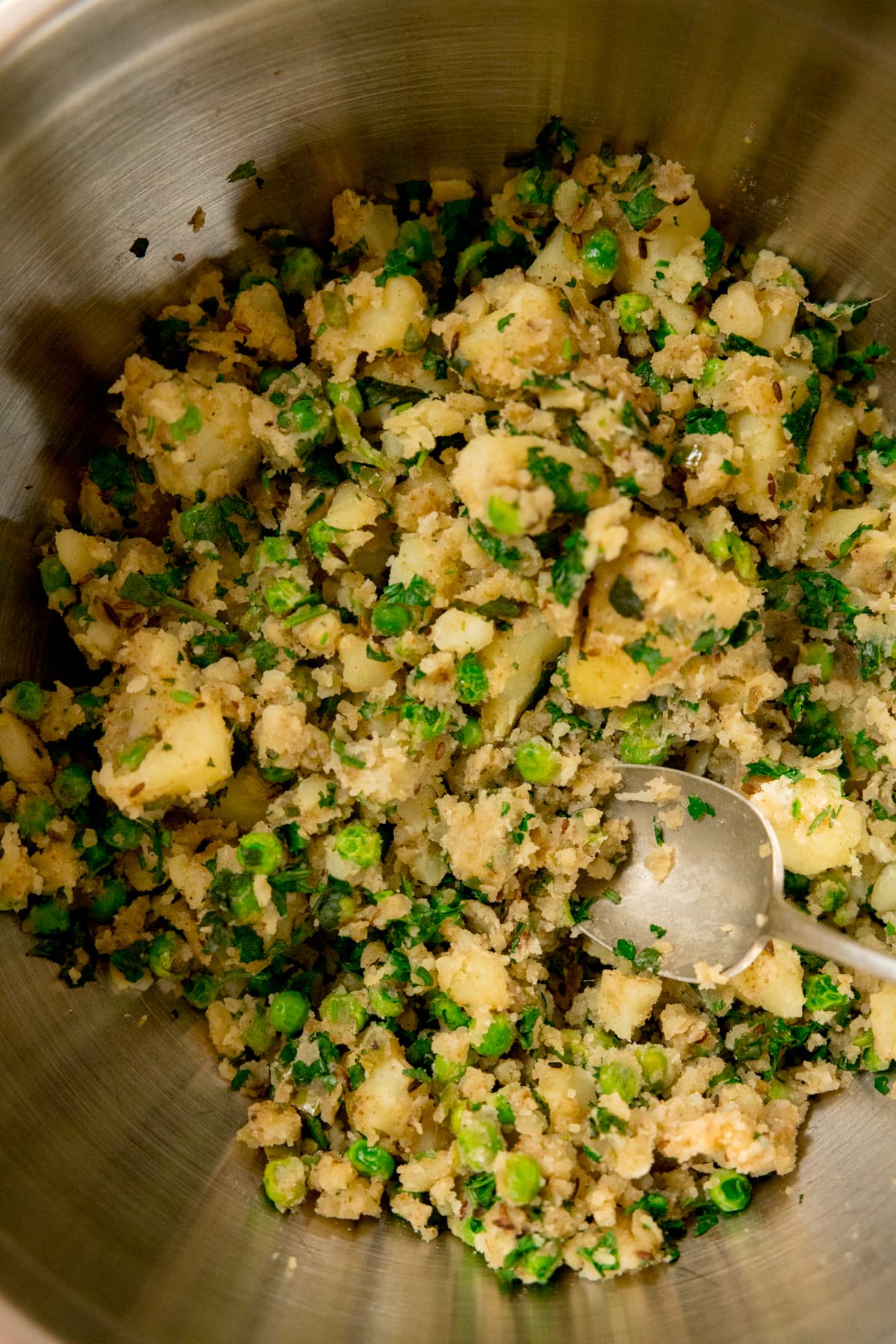 Close up picture of vegetable samosa filling in a bowl with a spoon in the foreground.