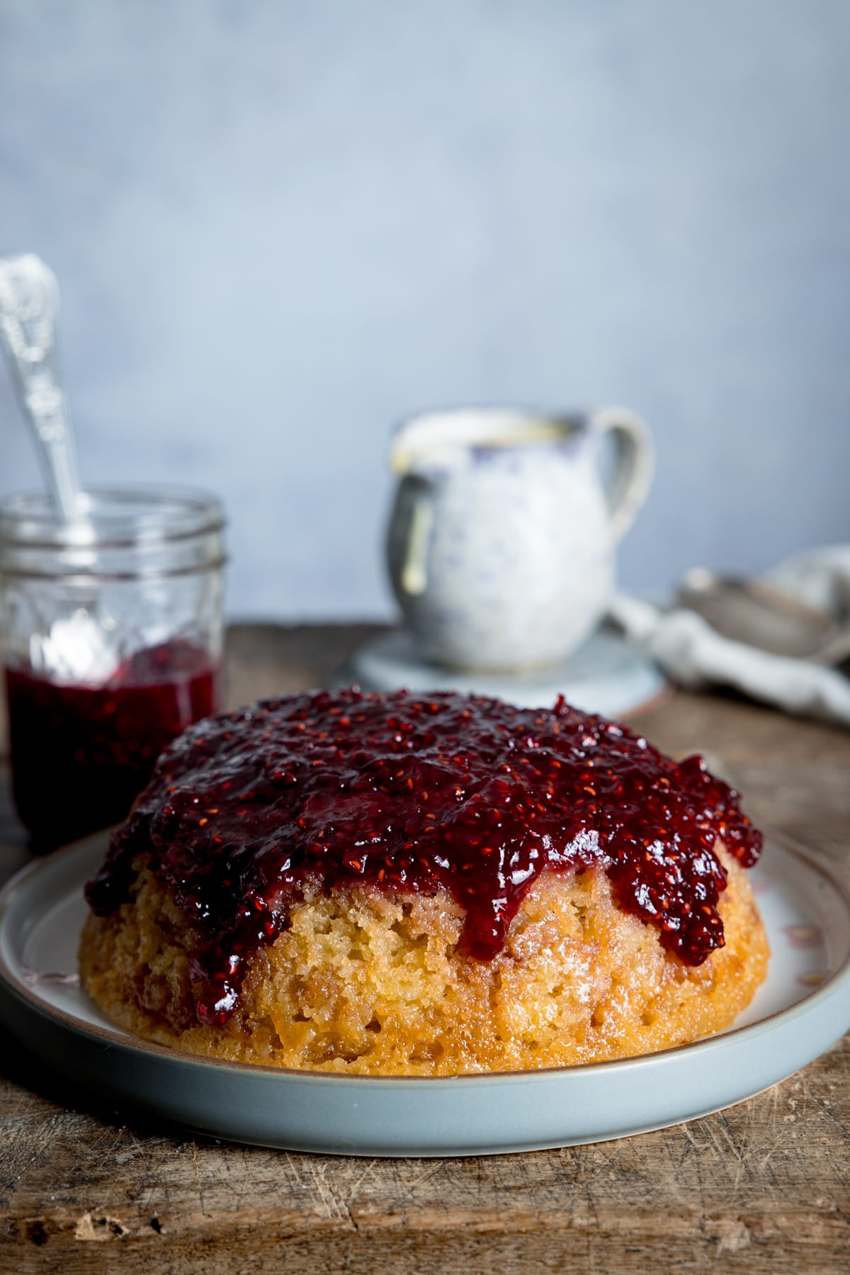 Picture of a steamed jam sponge on a grey plate thats sat on a wooden board.