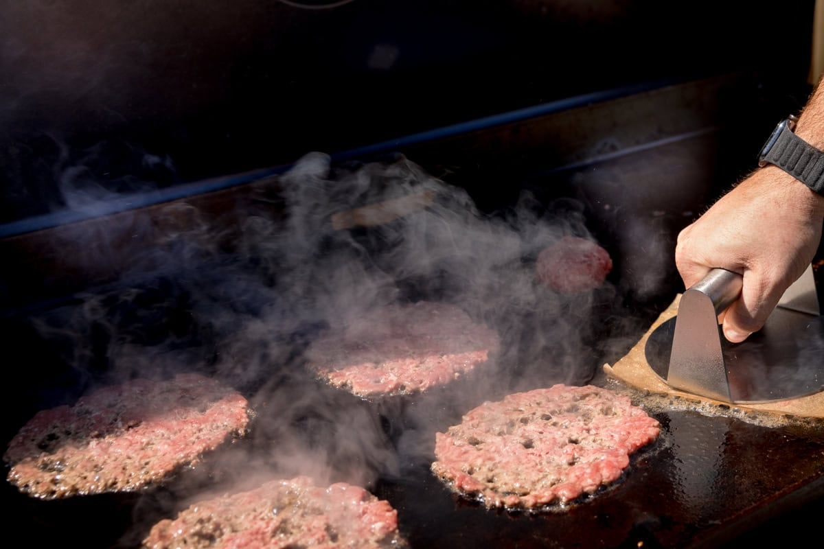 A wide process shot of Smash burgers cooking on the barbecue.