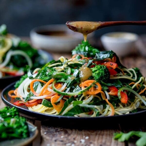 miso dressing being drizzled onto a noodle salad on a dark background