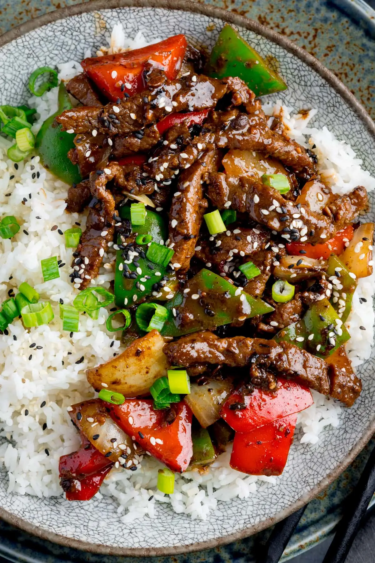 Beef in black bean sauce stir fry with boiled rice in a bowl, topped with spring onions and sesame seeds.