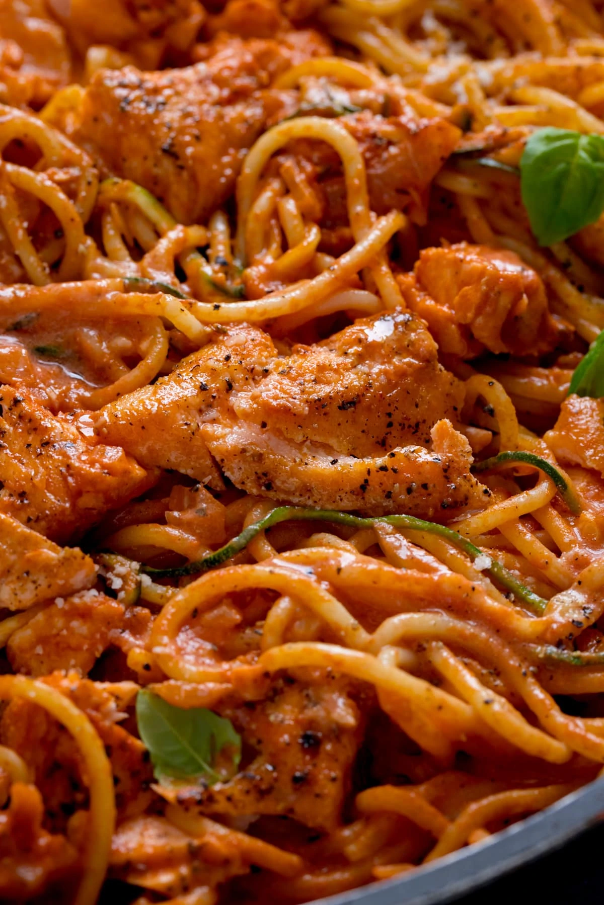 Close up of pieces of seasoned salmon in spaghetti in a creamy tomato sauce.