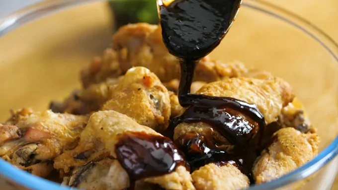 Sticky Asian sauce being poured over crispy chicken wings in a bowl