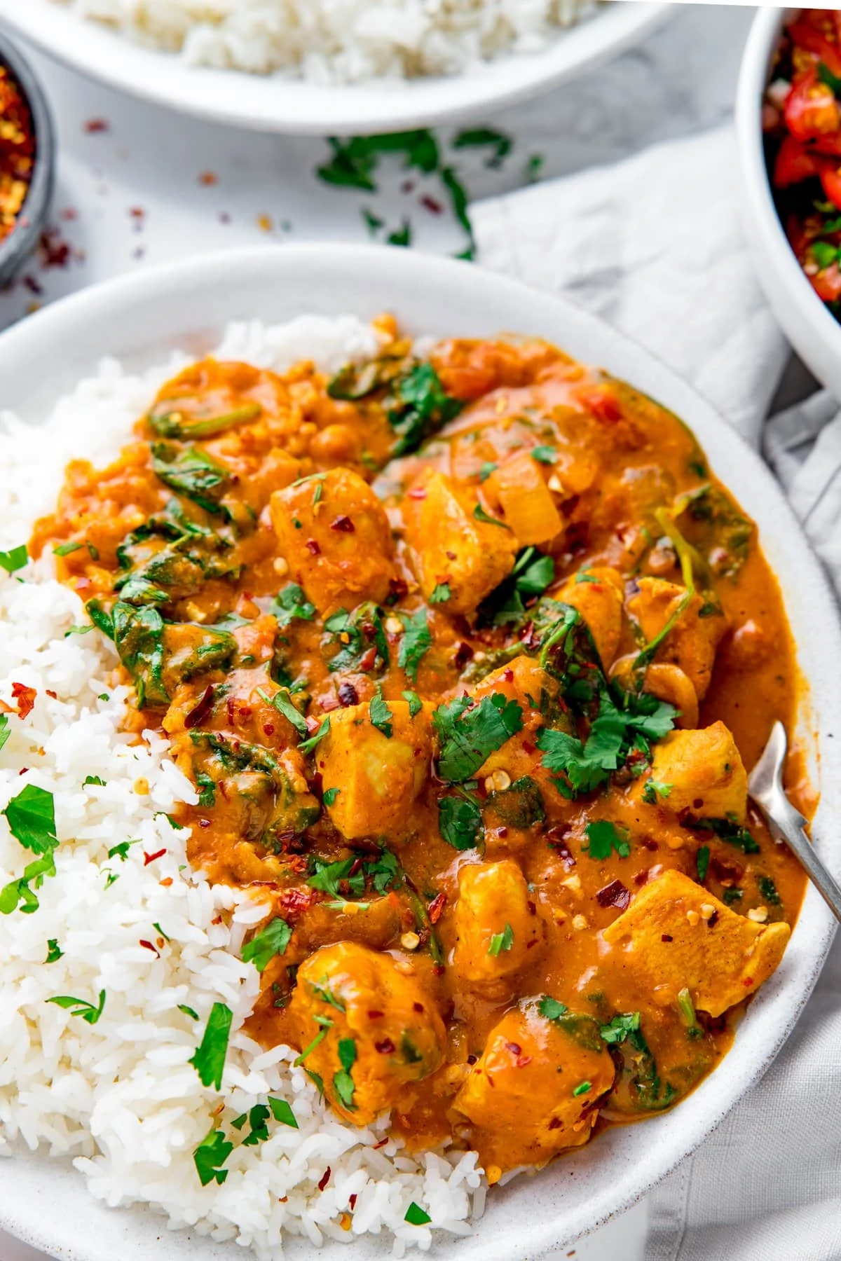 Close up of chicken curry and boiled rice in a white bowl topped off with chopped coriander.