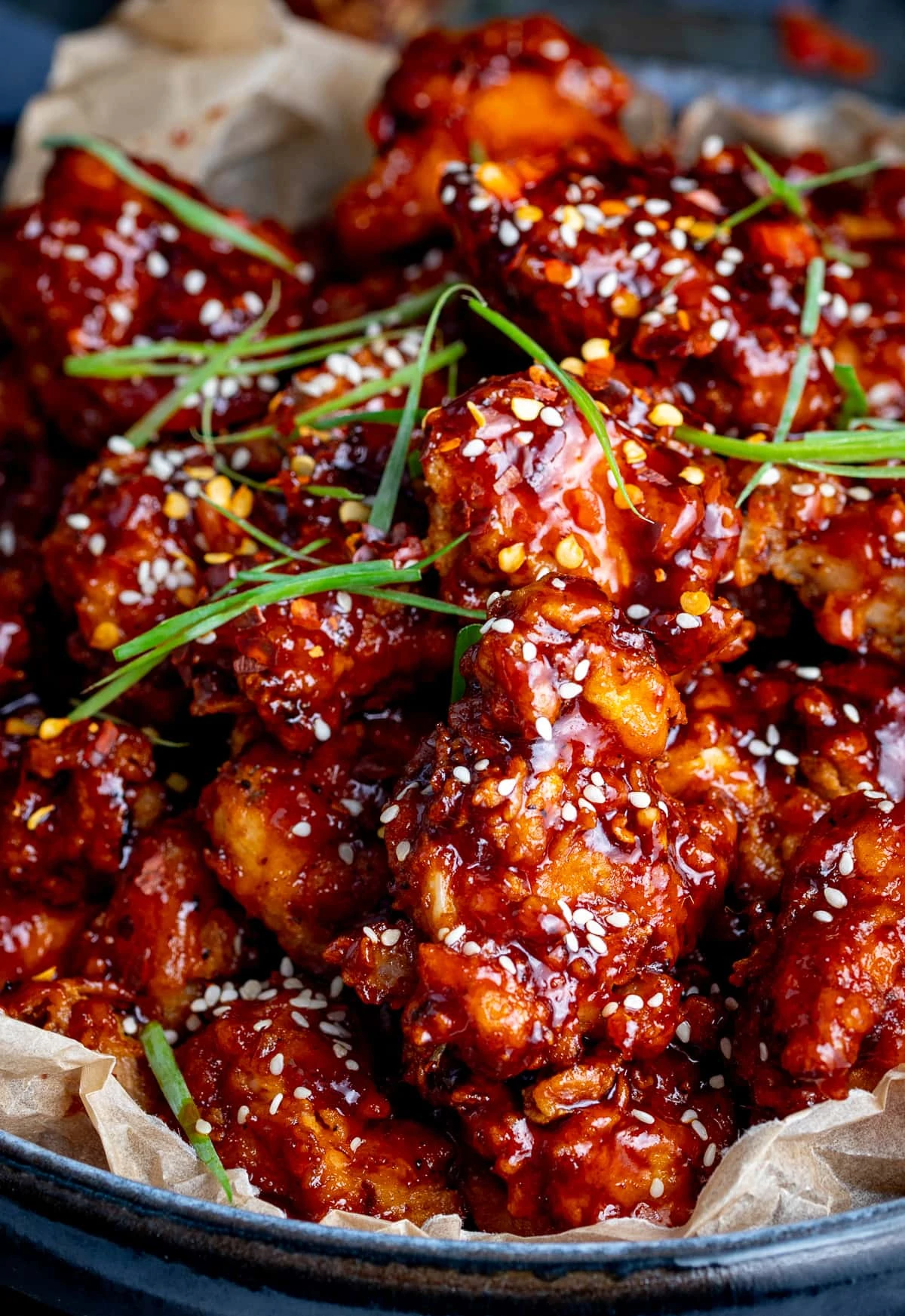 Close up shot of a bowl of Korean fried chicken topped with sesame seeds and strips of spring onion.