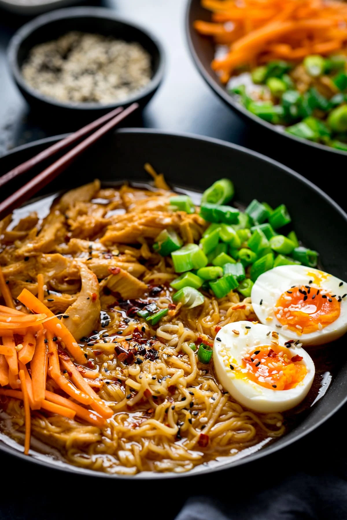 Bowl of chicken ramen with further bowl and a little bowl of sesame seeds in background.