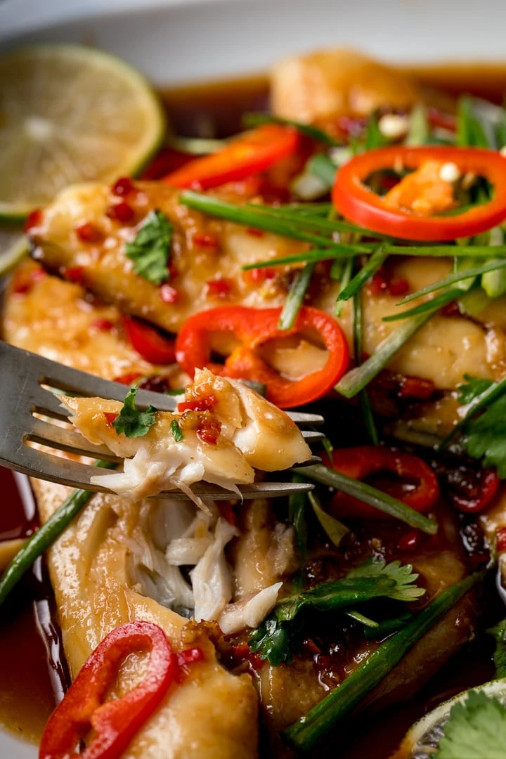 Forkful of sea bass being taken from a plate of sticky Asian sea bass